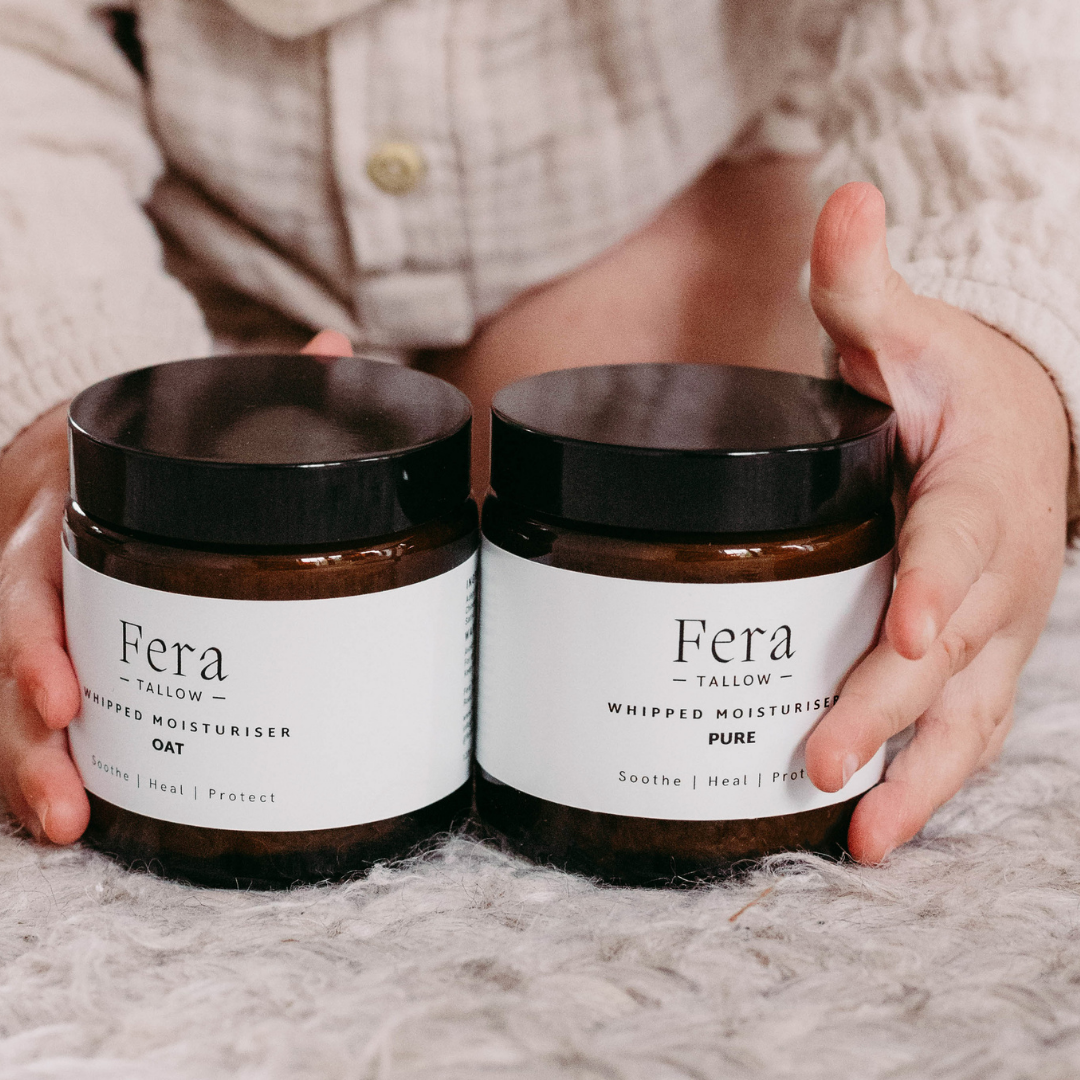 Two jars of tallow moisturiser held by a babies hands