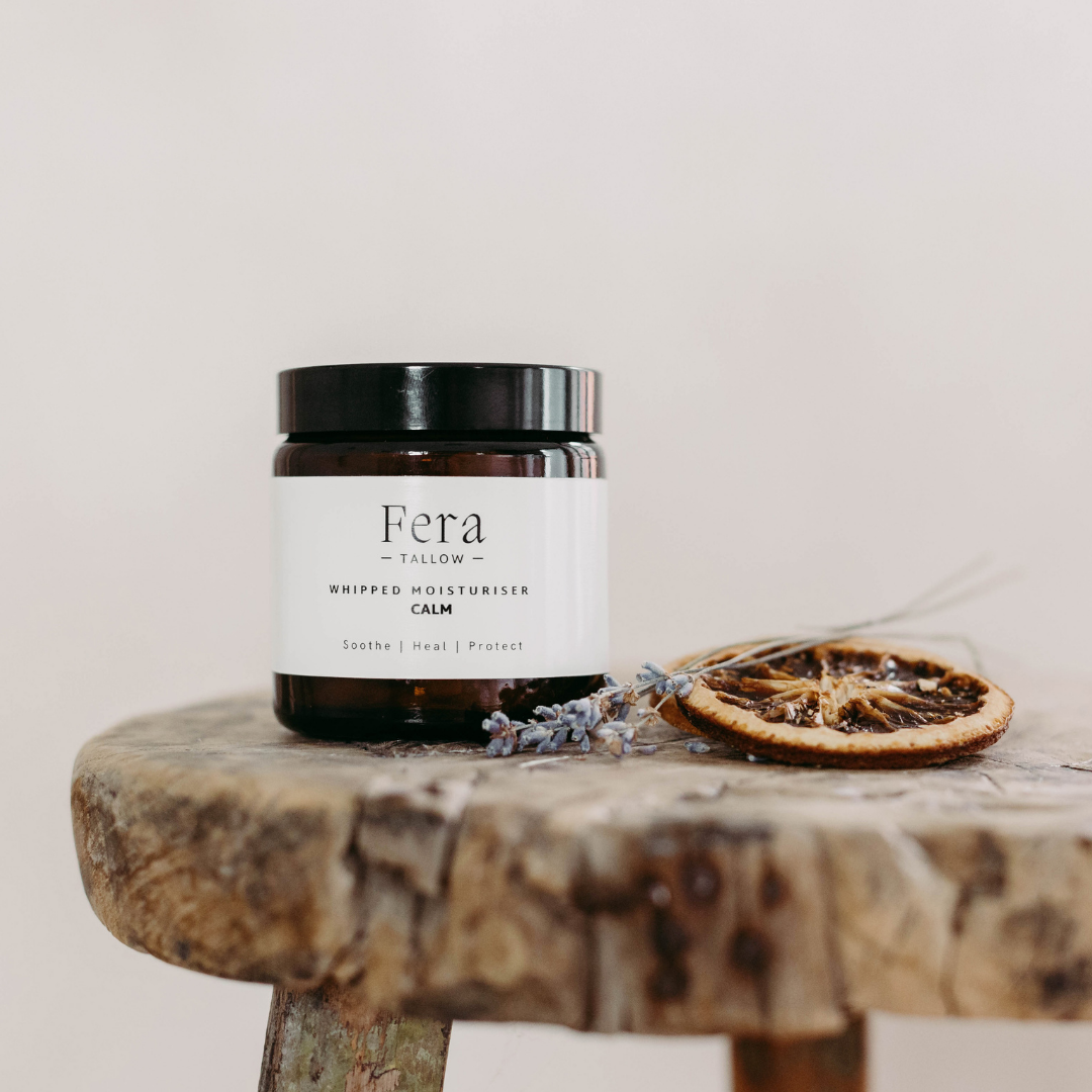 Fera whipped moisturiser jar on a wooden stool with dried oranges and lavender.