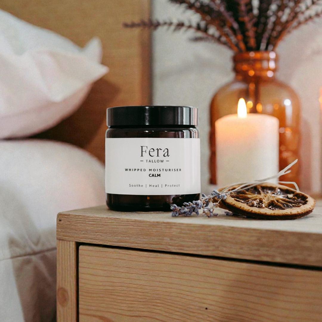 Fera whipped moisturizer jar on a wooden surface with a lit candle and decorative elements.